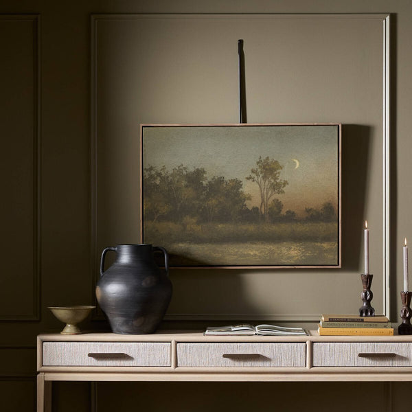 Framed landscape painting on a wall above a wooden console table with decorative items.