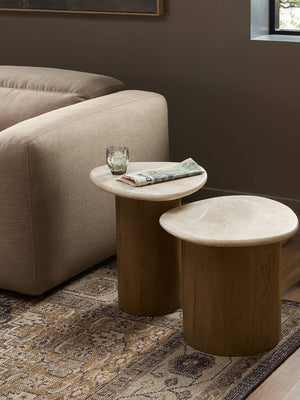 Two wooden side tables in front of a beige sofa with a glass and newspaper on one table.