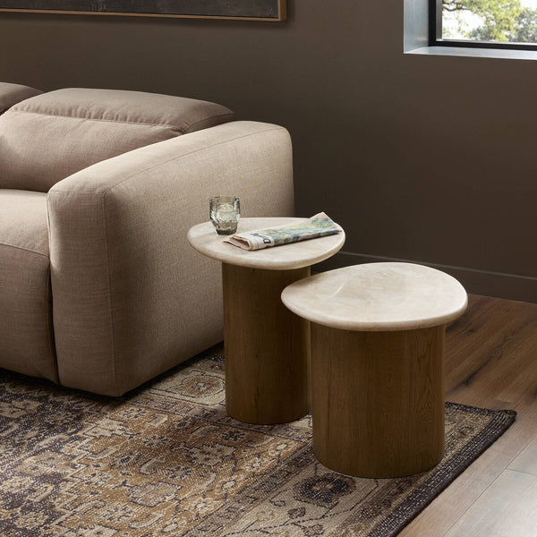 Two wooden side tables in front of a beige sofa with a glass and newspaper on one table.